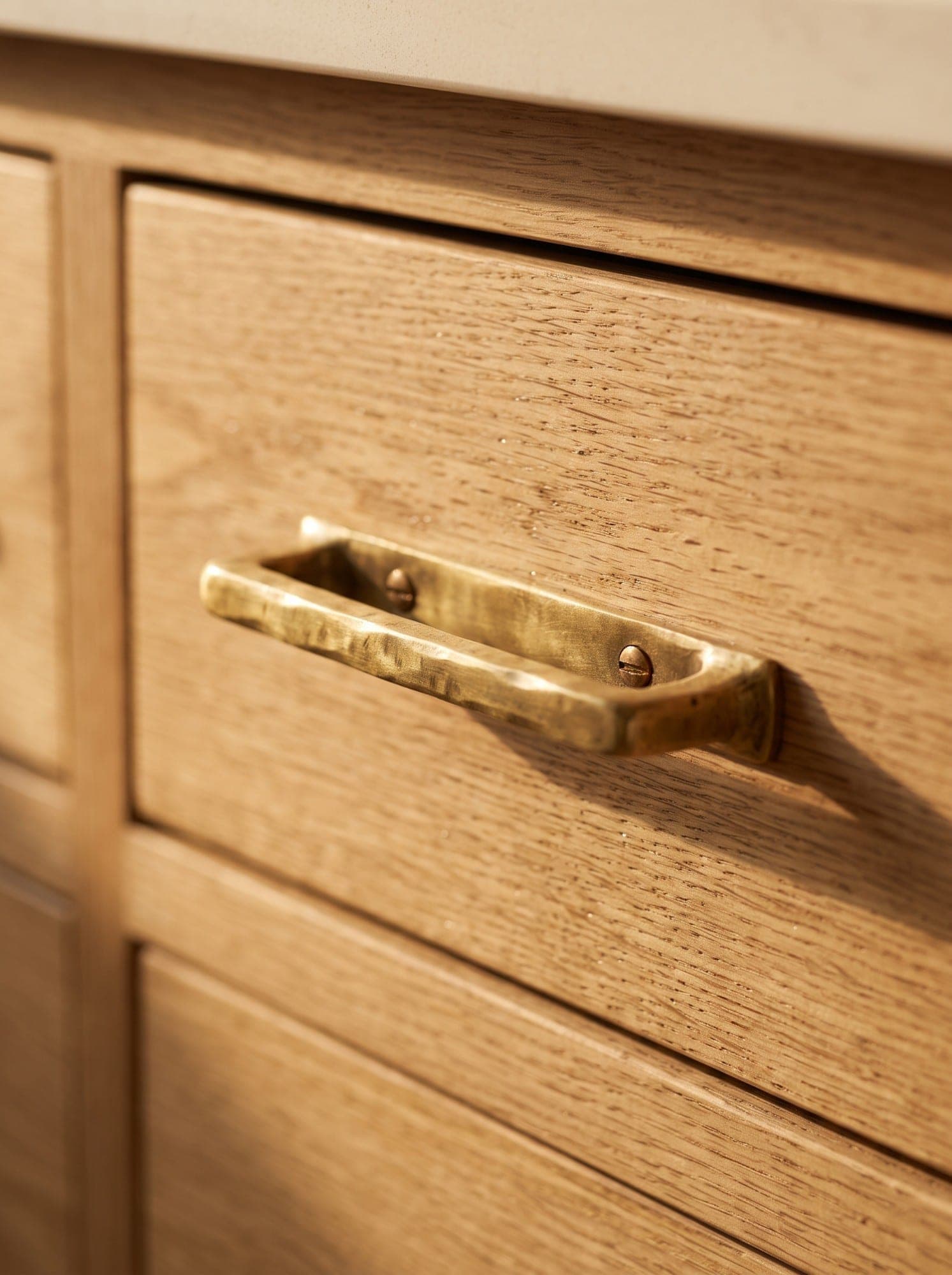 A hand-hammered brass pull on a white oak drawer in warm sunlight